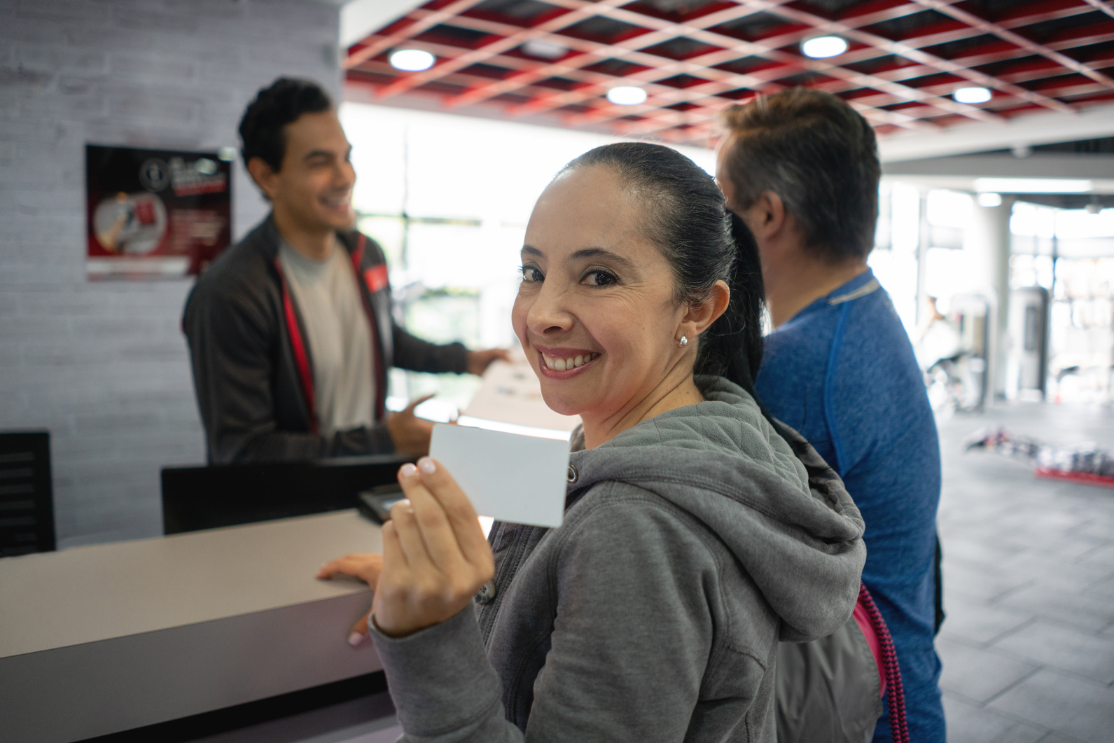 Happy adult woman holding a membership card for the gym facing camera smiling