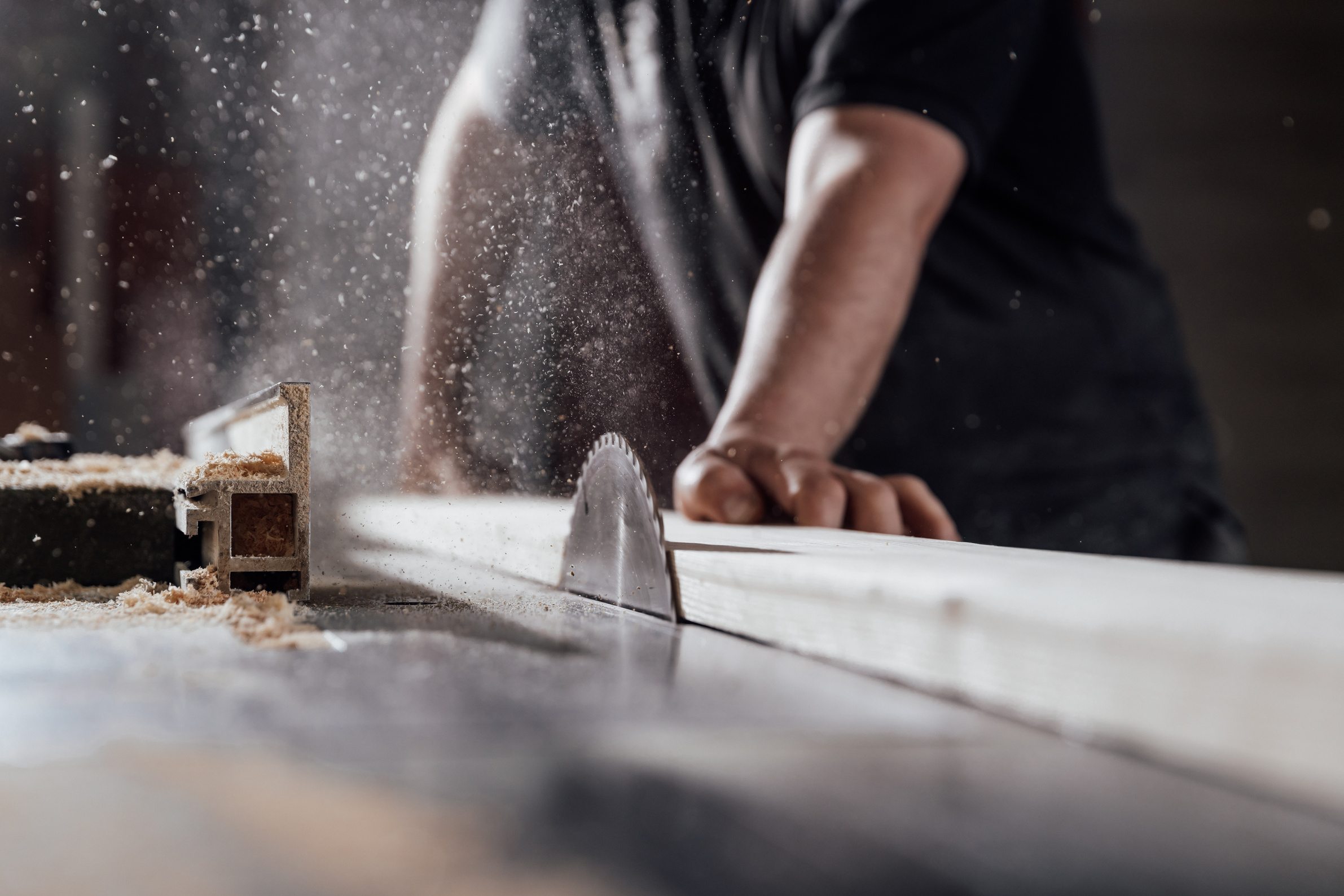 Midsection of carpenter cutting wood on table saw in workshop
